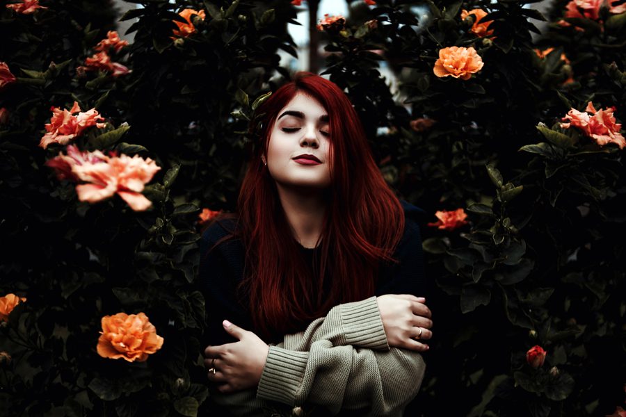woman with red hair and matching makeup surrounded by flowering bushes