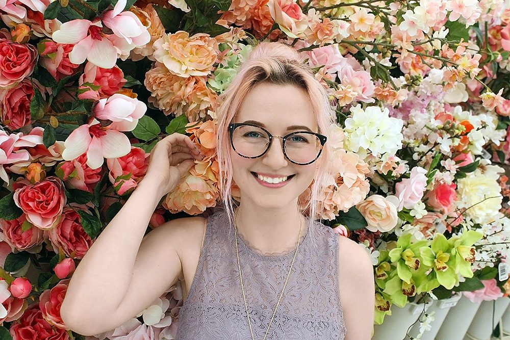 Spring hair care concept - young woman with glasses with colorful flowers behind her