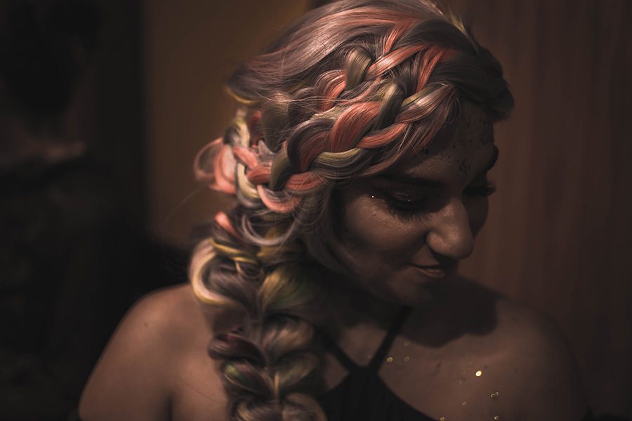 halloween hairstyle - woman with multicolored braids and glitter in a dark room