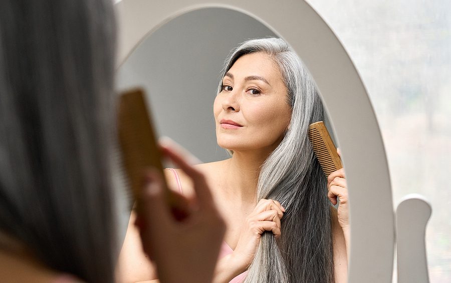 Senior asian woman with gray hair combing it in front of a mirror. gray hair concept
