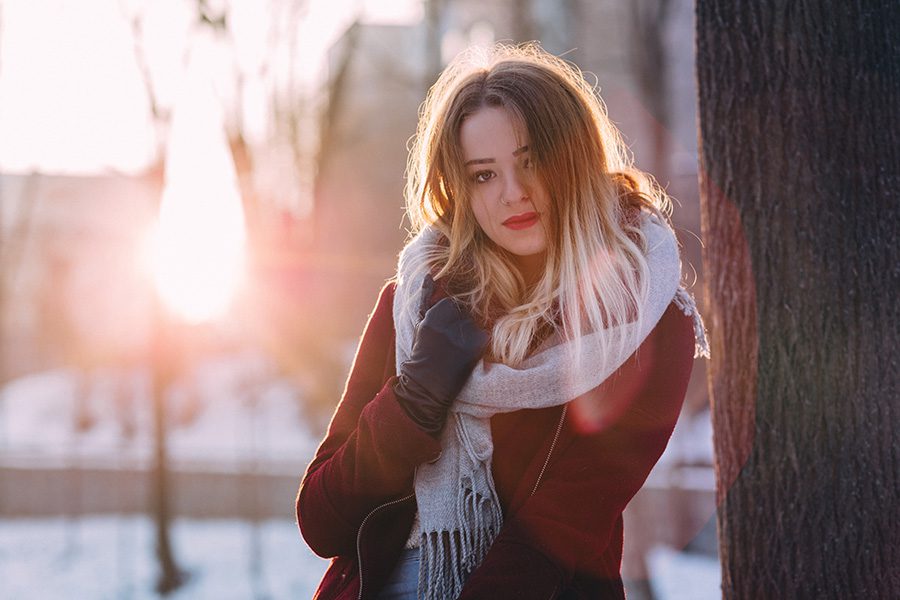 Young woman leaning on tree in the winter, hair blowing in wind - winter dry scalp hair care concept