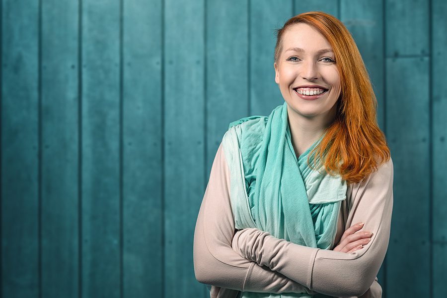 woman with red hair and side undercut standing and smiling against a blue background