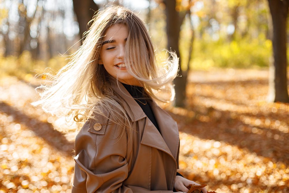 young woman twirling hair in a park in the fall - restoring hair health after summer concept