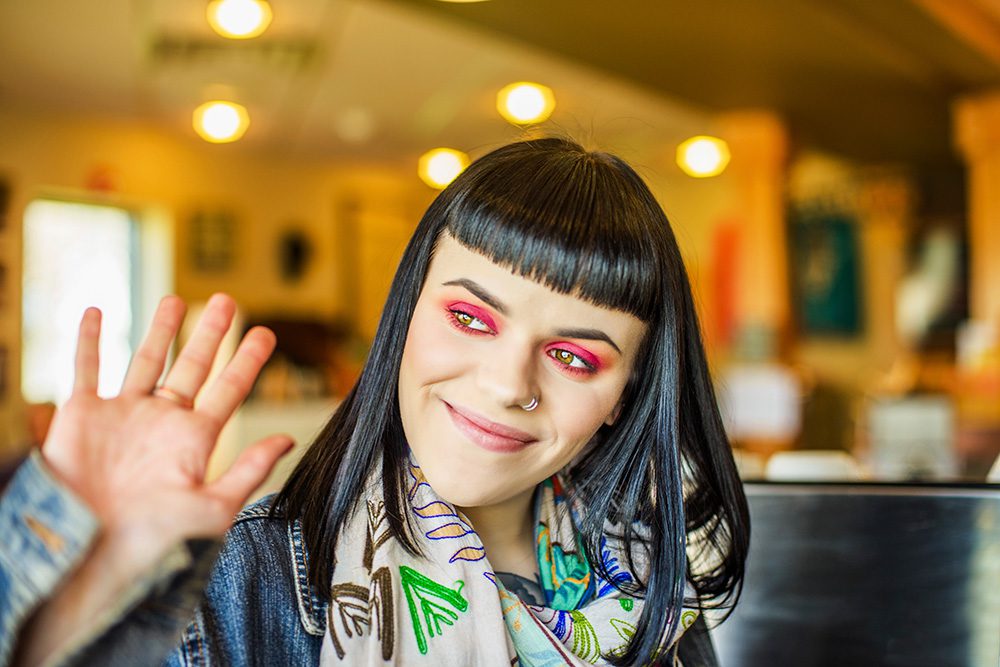 young woman with micro bangs waving to someone out of frame