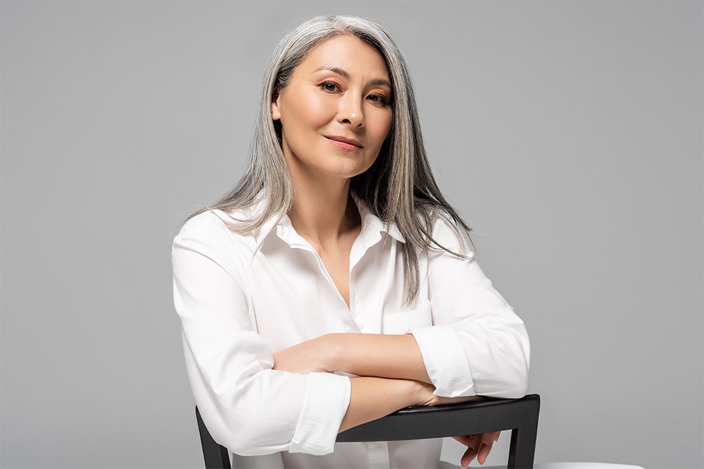 woman with gray hair leaning against a chair